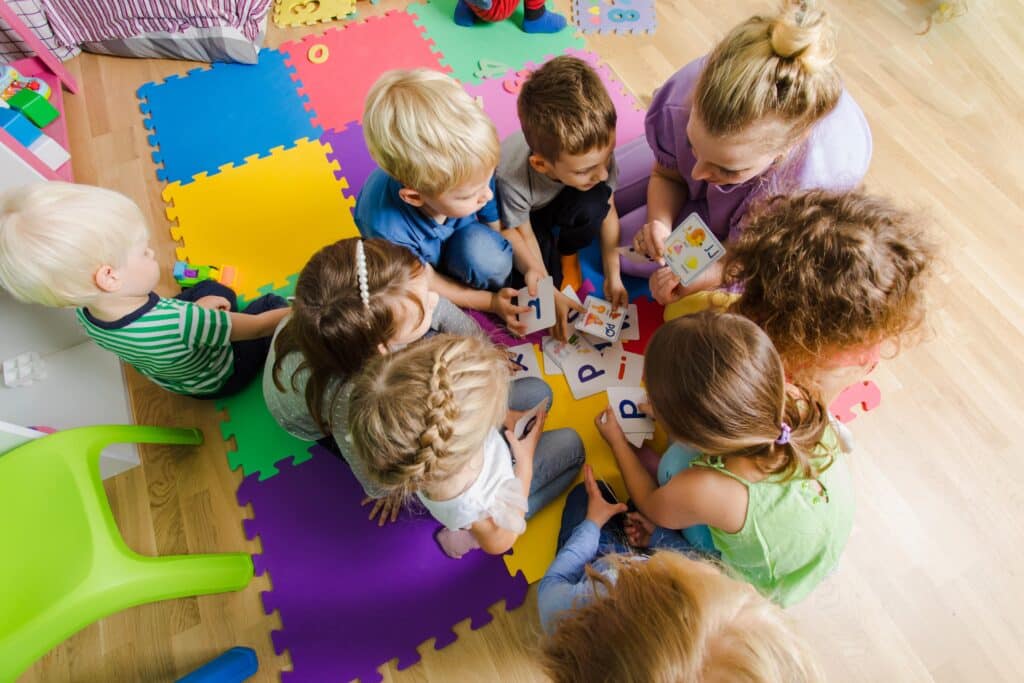 Der Übergang zwischen Kita und Grundschule: Kinder spielen mit Erzieherin auf dem Boden