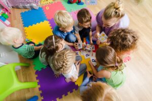 Der Übergang zwischen Kita und Grundschule: Kinder spielen mit Erzieherin auf dem Boden