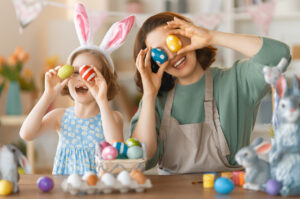 Ostern in Kindergarten und Kita – Erzieher/in und Kind halten bunt bemalte Ostereier vor ihre Augen