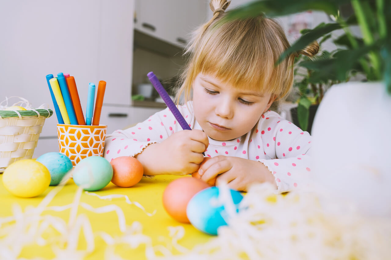 Ostern in Kindergarten und Kita - Ein Kind bemalt mit einem Filzstift mehrere eingefärbte Ostereier 