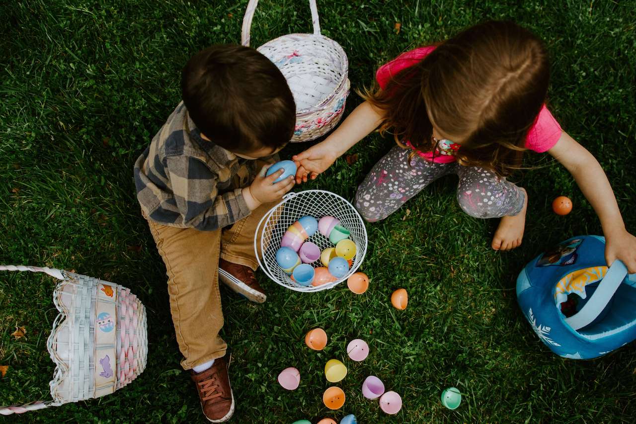 Ostern in Kindergarten und Kita – Zwei Kinder sitzen auf der Wiese und sortieren Ostereier in ihre Körbchen