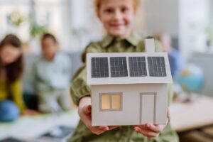 Nachhaltigkeit in der Schule - Mädchen zeigt gebasteltes Haus mit Solarpanels